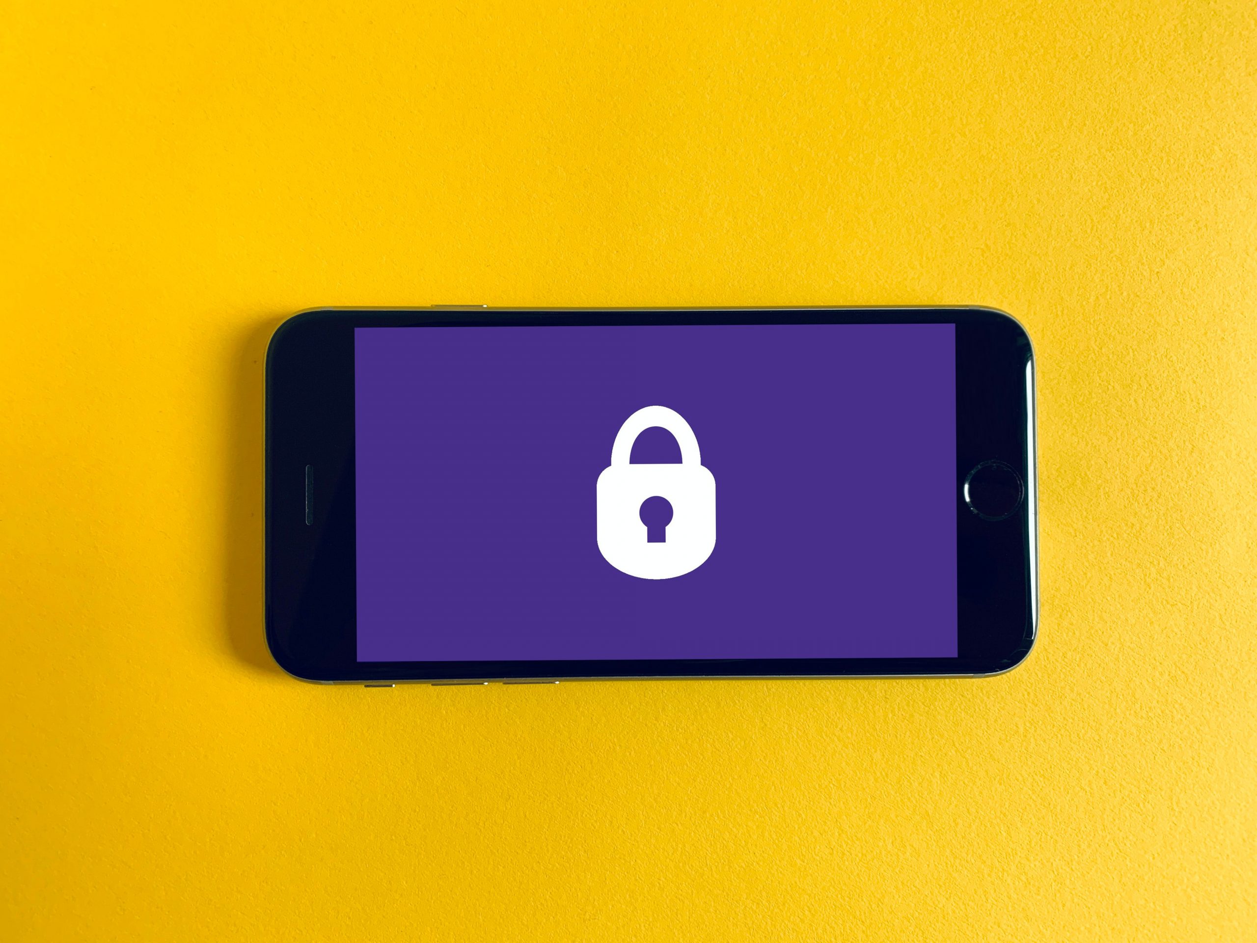 Mobiltelefon mit Vorhängeschlossdarstellung auf gelbem Hintergrund. Symbolisiert Datensicherheit.